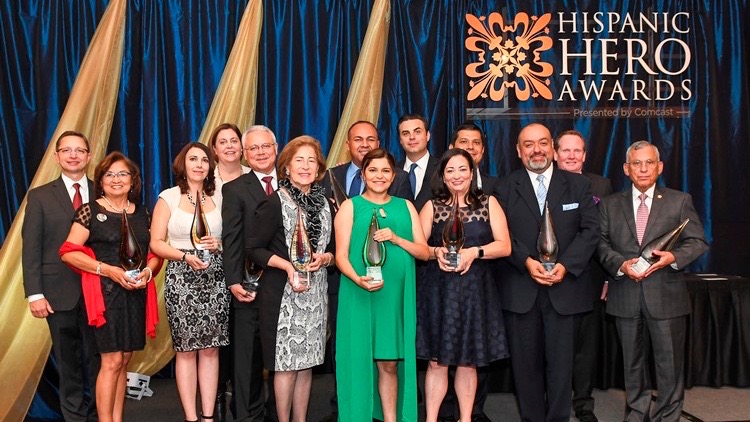 A group of people posing for a photo in front of a large Hispanic Hero Awards logo.