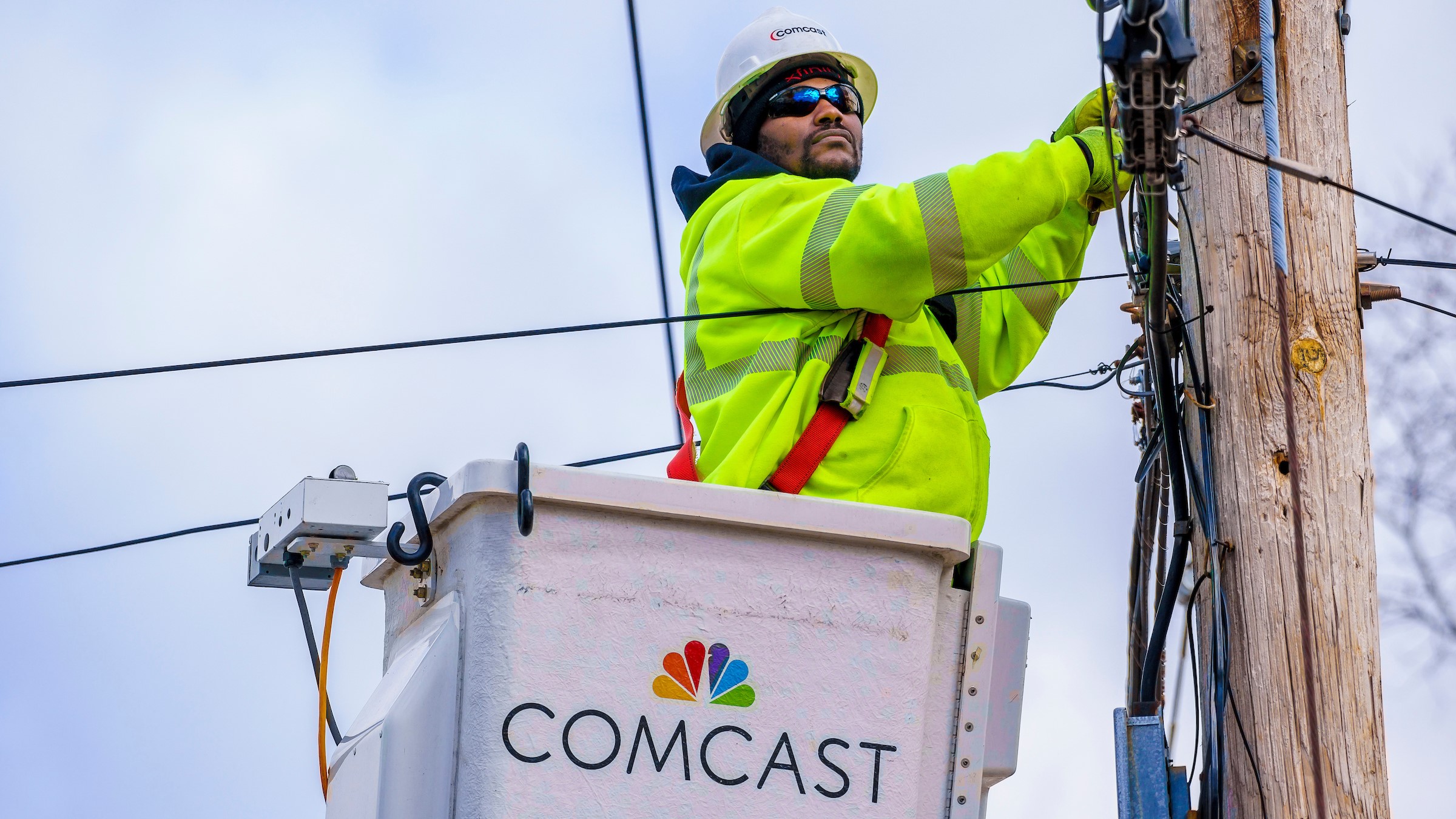 A Comcast lineman examines a cable line on a telephone pole.