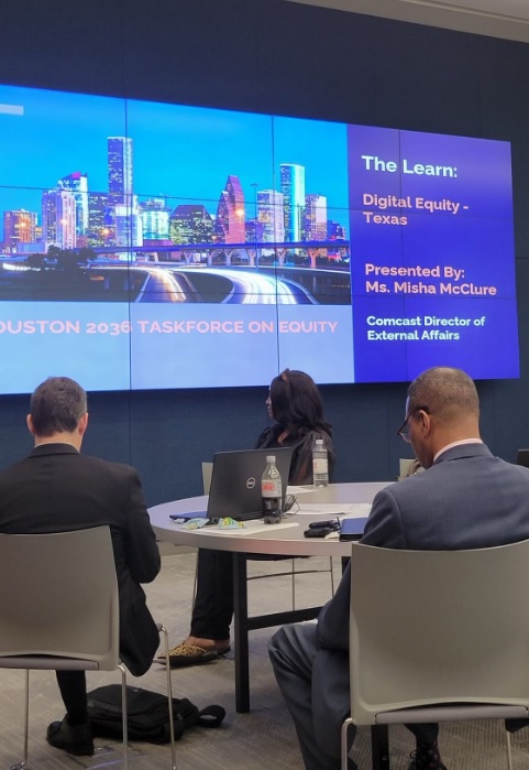 People sitting at a table looking up at large screen featuring Digital Equity Texas