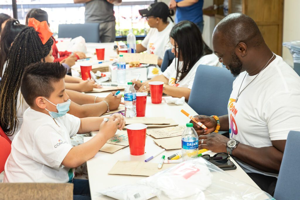 Group of volunteers seated at a long table and decorating paper lunch bags