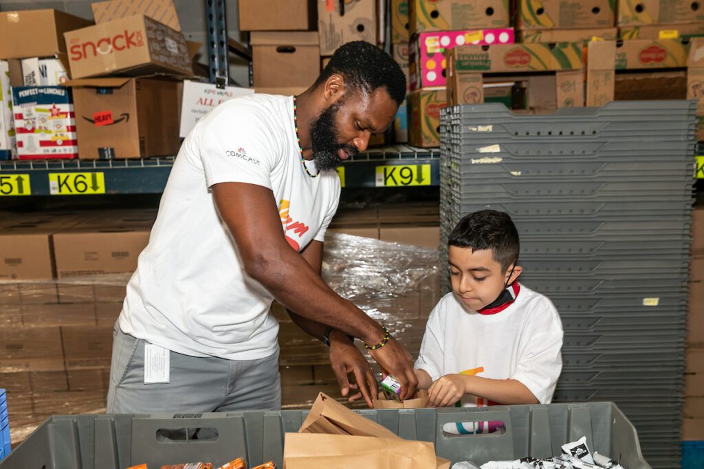 Man assisting young boy add items into a bag