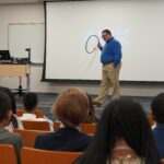 Speaker in front of room of seated children holding up cable fiber