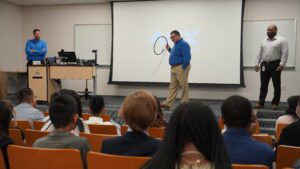 Speaker in front of room of seated children holding up cable fiber