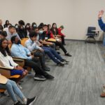 Man standing in front of group of seated children and explaining the able fiber he holds up