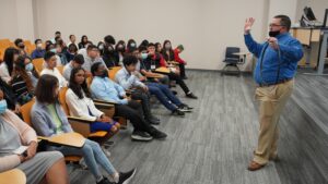 Man standing in front of group of seated children and explaining the able fiber he holds up