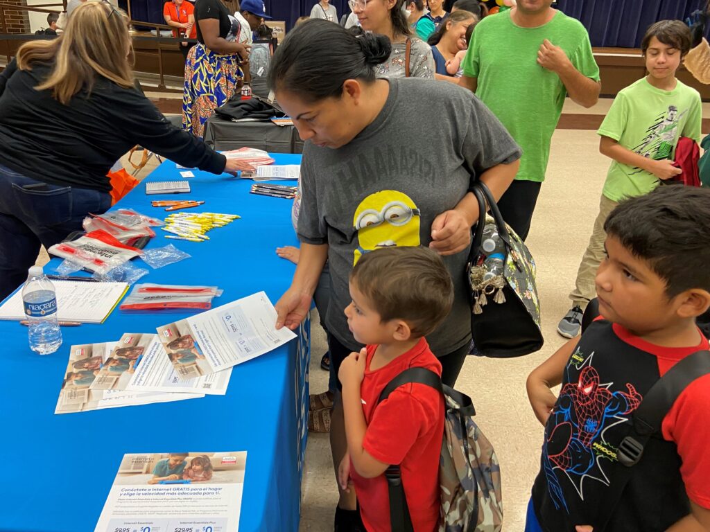 A woman and two young boys peruse a table containing information