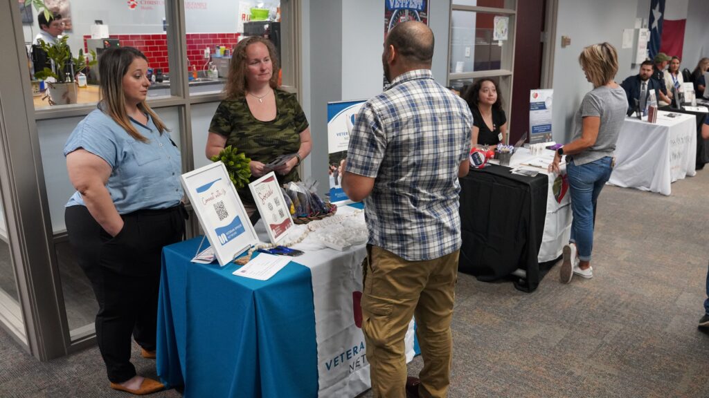 Two women standing behind table and speaking to a gentleman