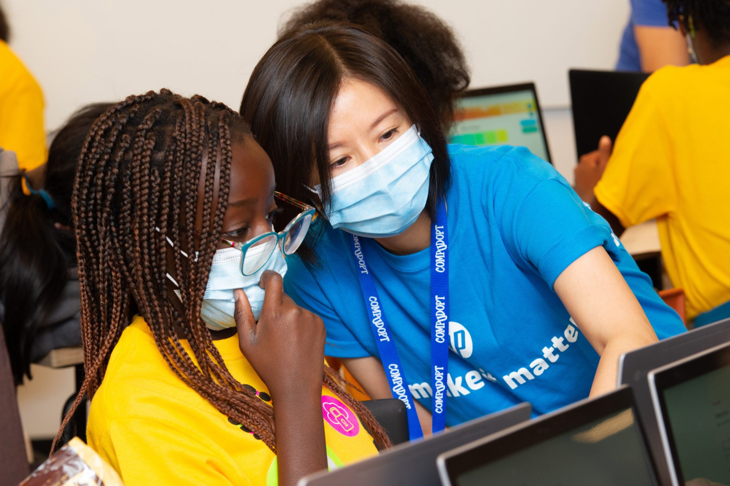 A woman leaning over to help young student with laptop