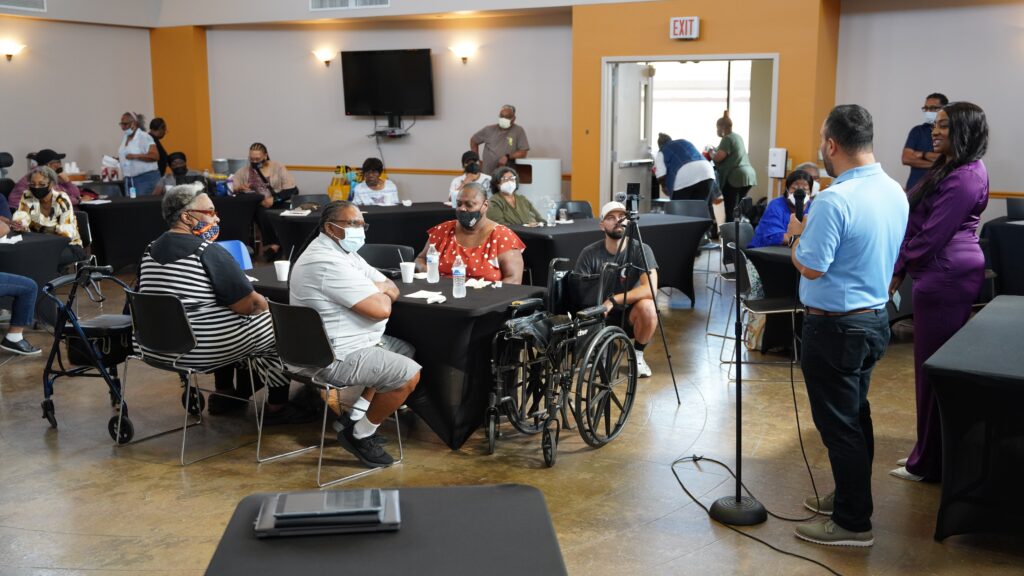 Man at a microphone speaking to people seated at tables.