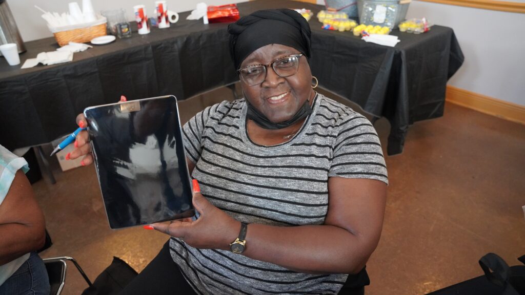 A woman wearing grey and black striped shirt smiling and holding tablet