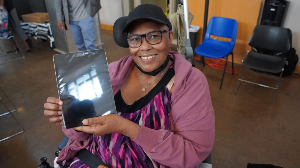 Smiling woman in black hat and purple sweater holding tablet