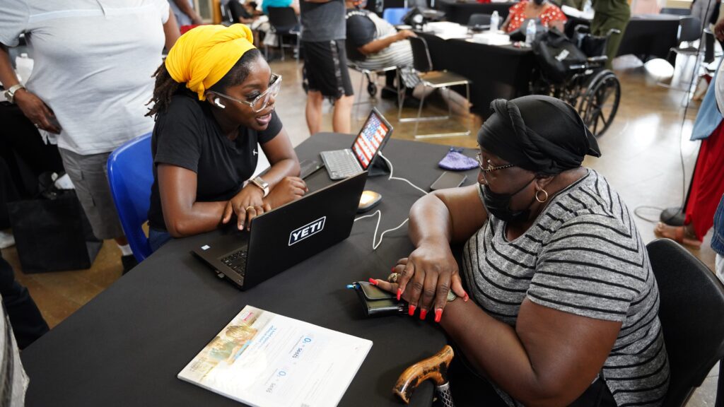 A woman sitting with laptop speaking with older woman across a table.