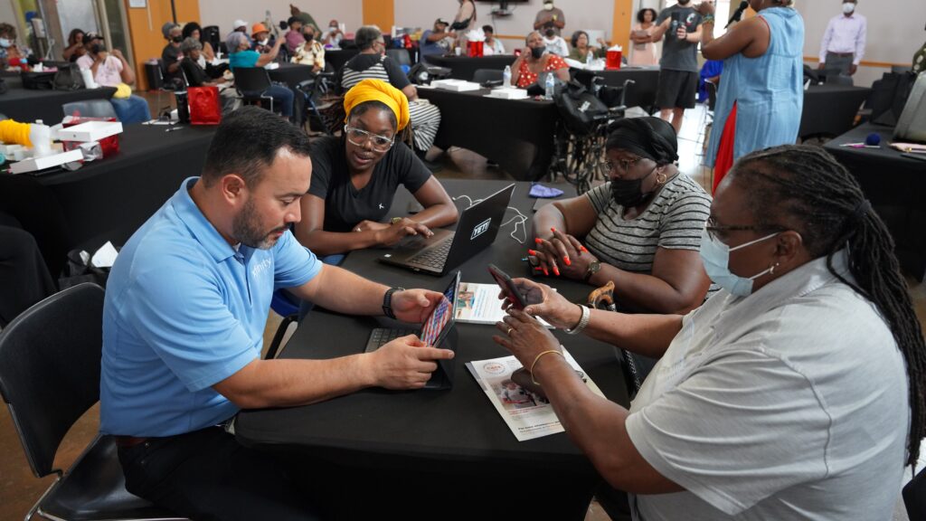 People seated at a table discussing multiple electronic devices.