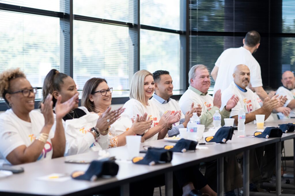 Group of people wearing Team Up t-shirts sitting behind long table and clapping