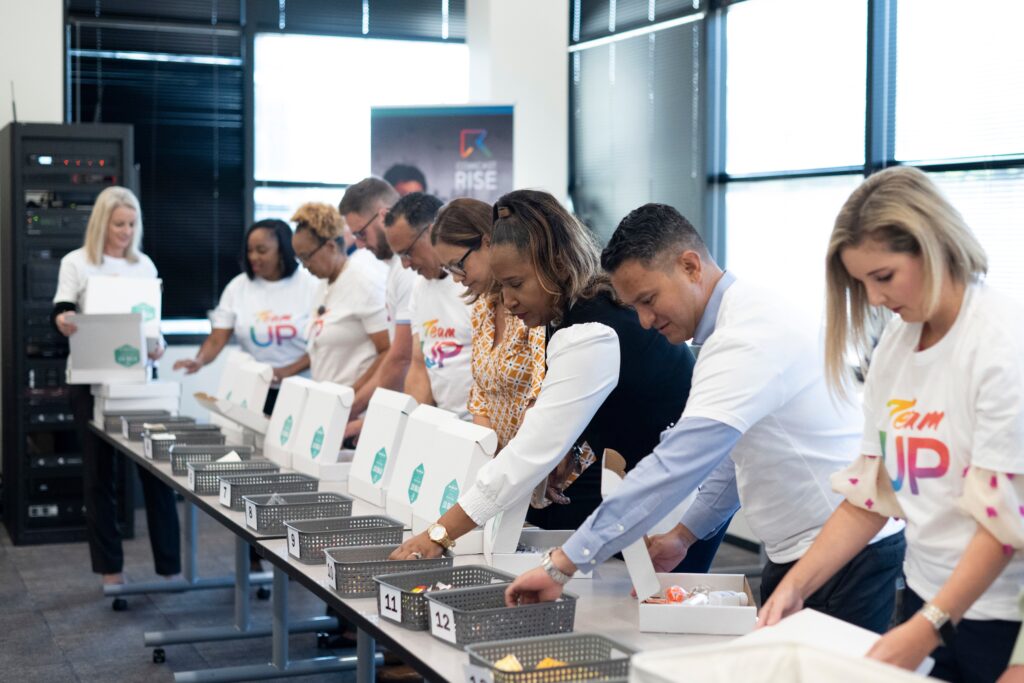 Volunteers standing behind long table adding items to small boxes