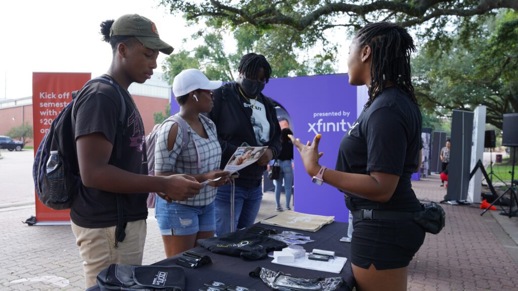 Students speaking with young woman at booth table