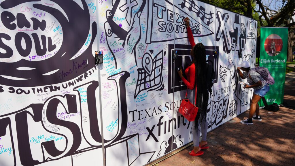 Two students writing messages on signature wall