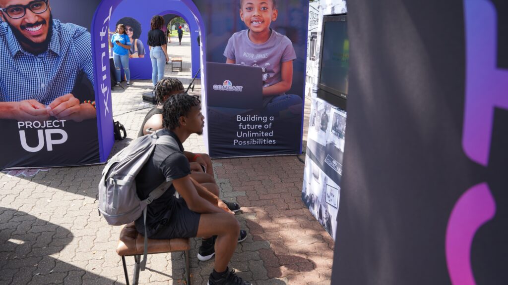 Two students sitting on a bench watching information on a large flat screen