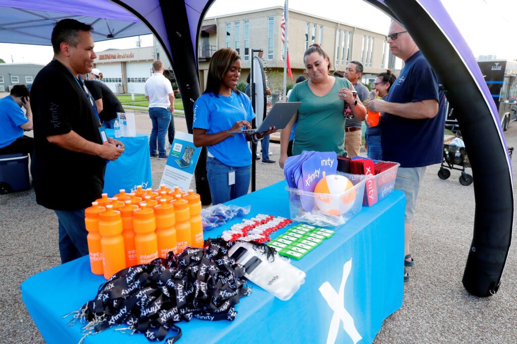 Xfinity volunteers speaking with a couple at an information table