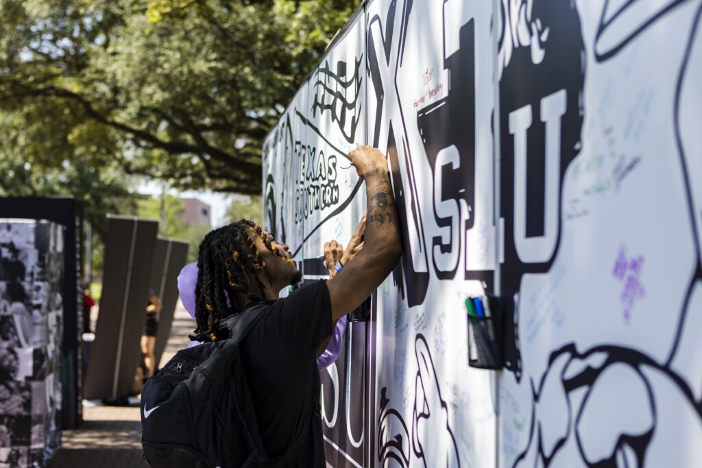 Student wearing backpack adding message to signature wall