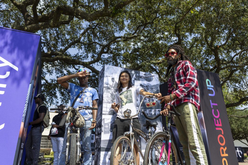 Three students with bikes standing near Xfinity and Project Up signs