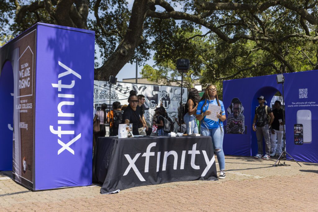 Students standing behind Xfinity table with clip boards