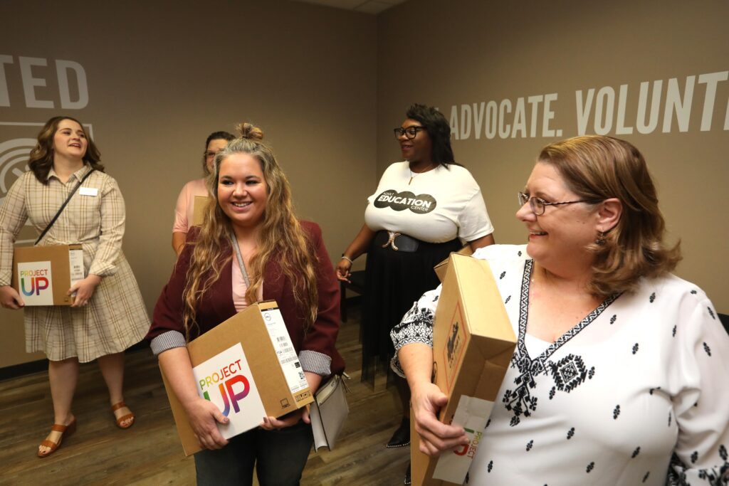 Multiple women standing around holding laptop boxes with Project Up logos