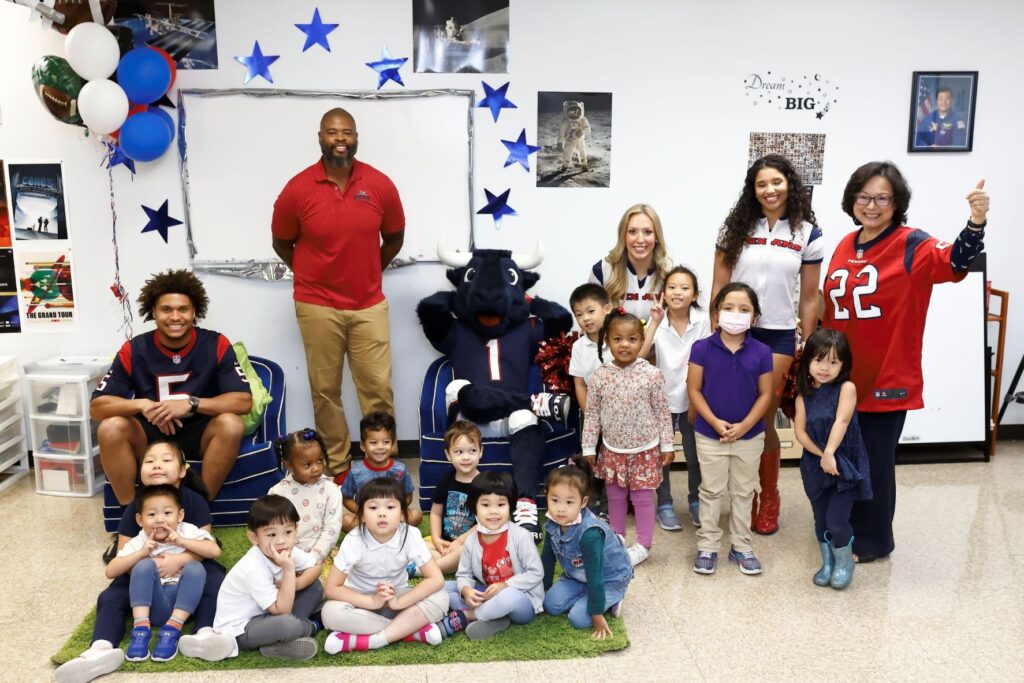 Group of young children and volunteers posing for picture at the front of a classroom