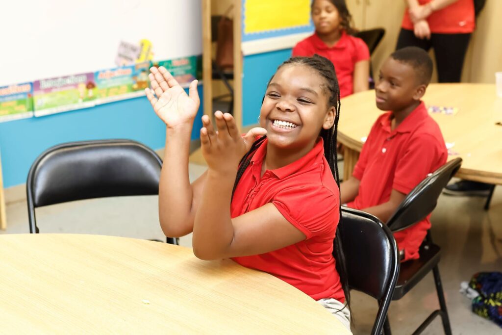 Young girls wearing red shirt seated at table smiling and clapping