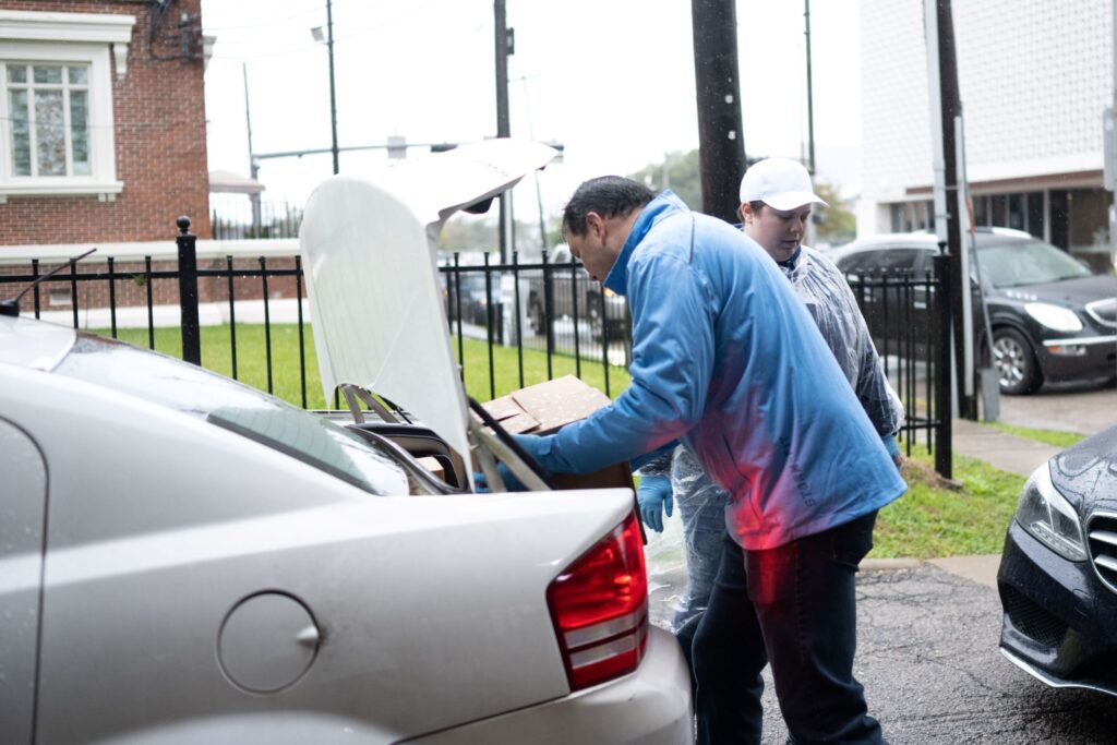 Gentleman wearing blue sweater putting a box in a car trunk.