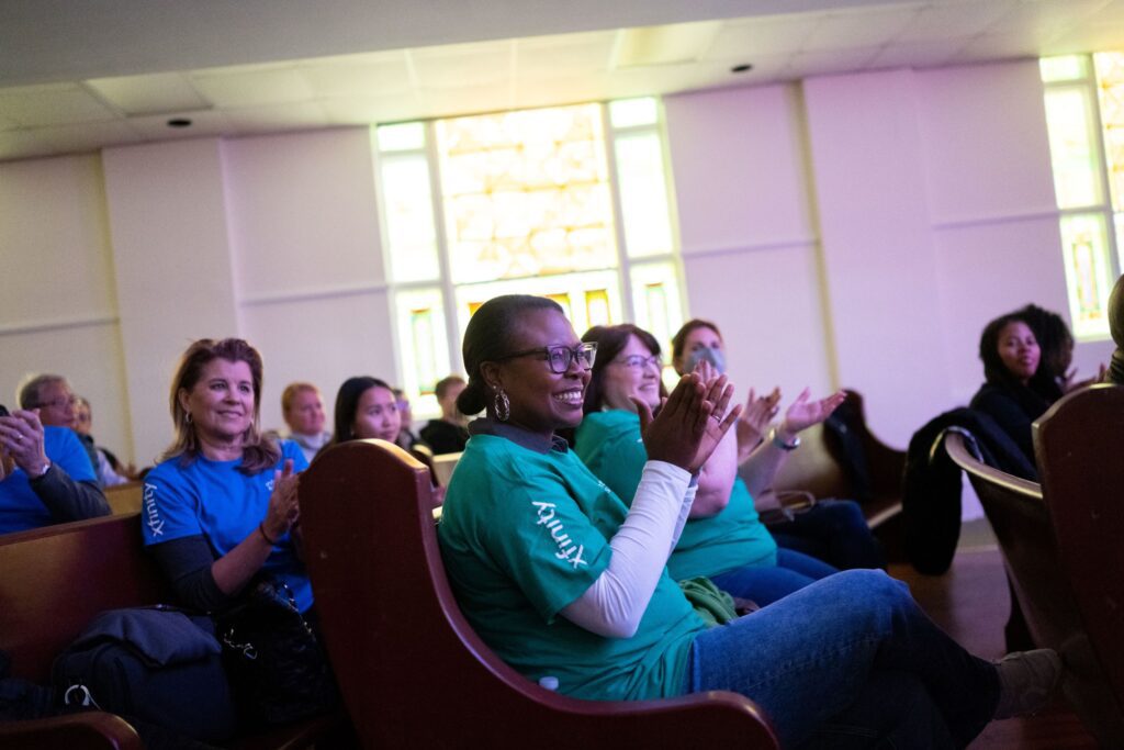 Multiple guests sitting in church pews wearing Xfinity t-shirts