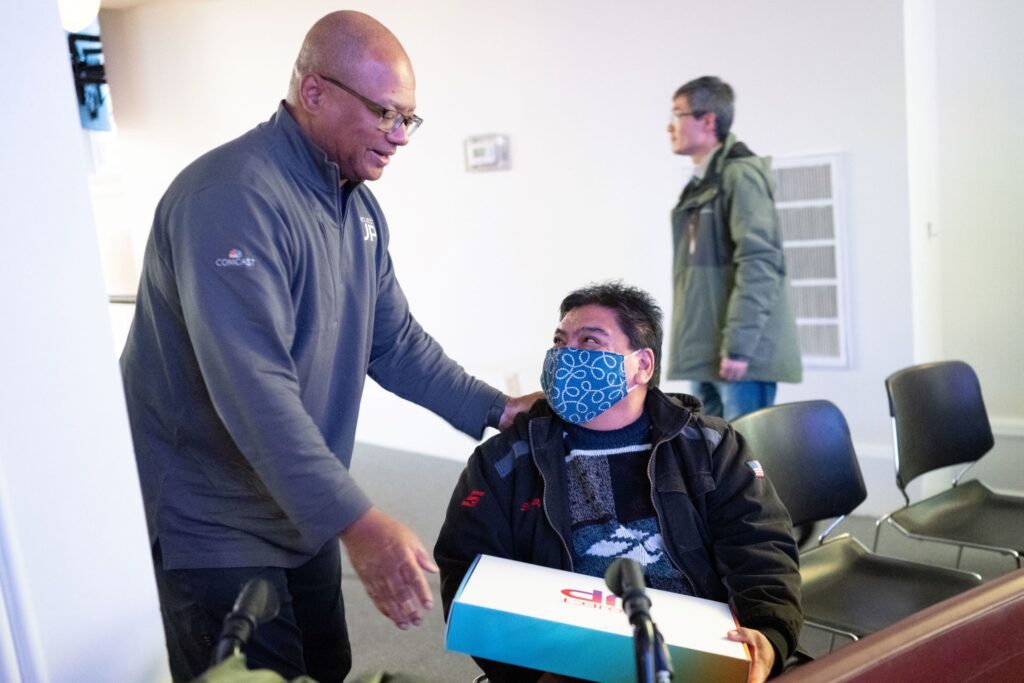 Broderick Johnson speaking to seated gentleman wearing mask and holding Team Up box.