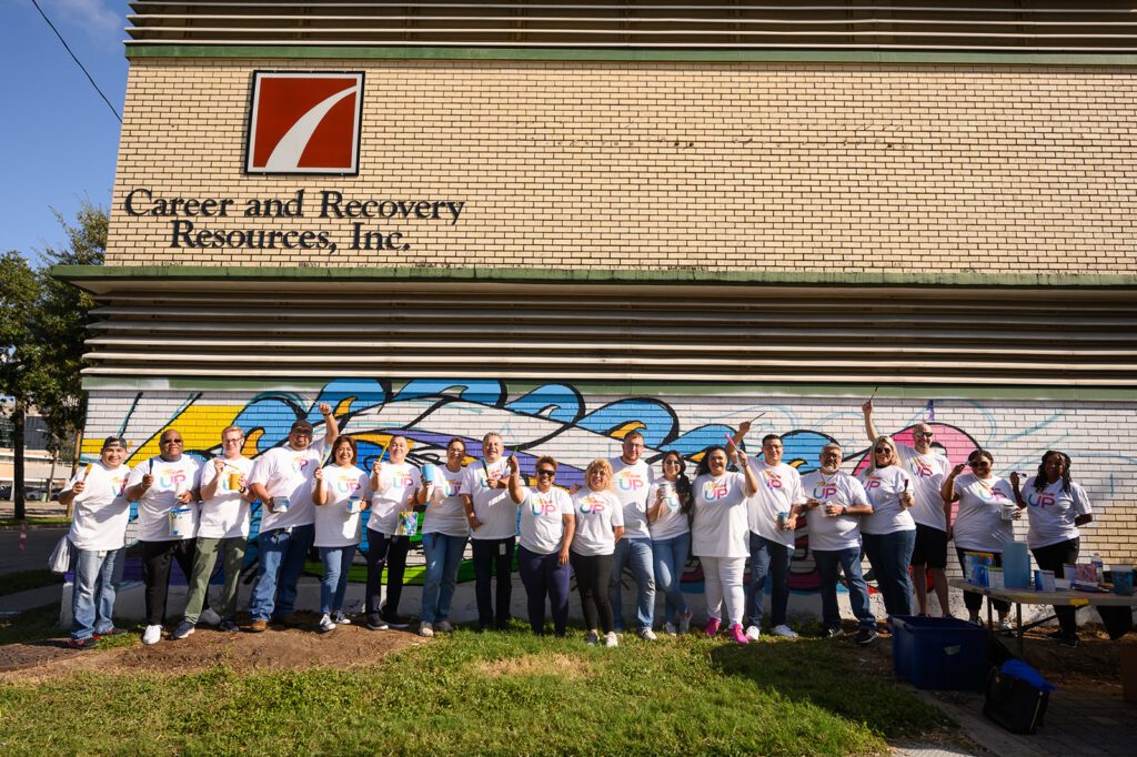 Large group of volunteers painting mural on brick building