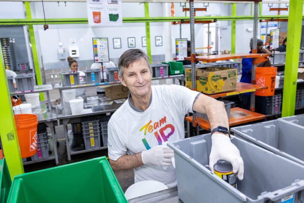 Team Up volunteer adding large can to bin at Houston food bank.