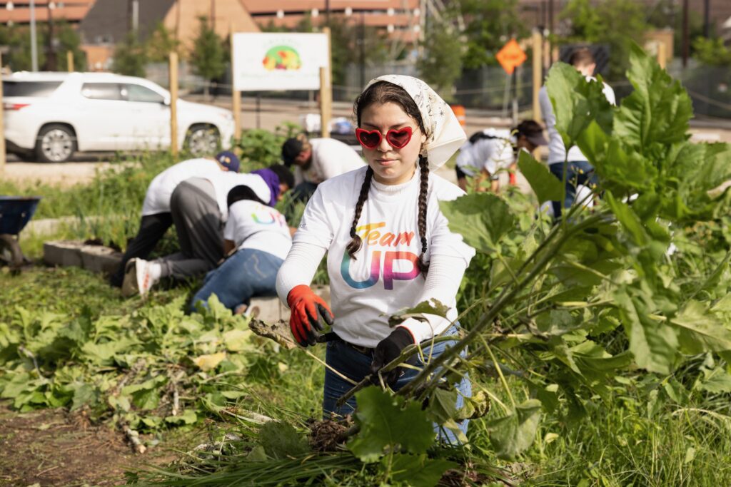 A volunteer with braids and red heart sunglasses weeding in garden