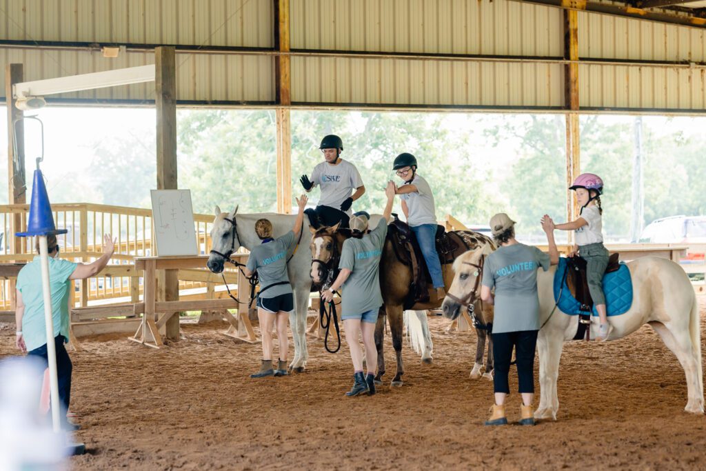 Three horses with their riders receiving high fives from trainers