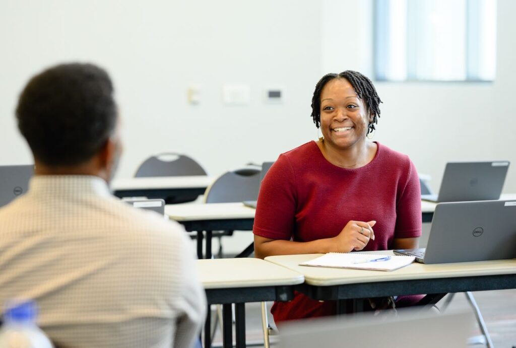 A woman is seen smiling in front of a computer.