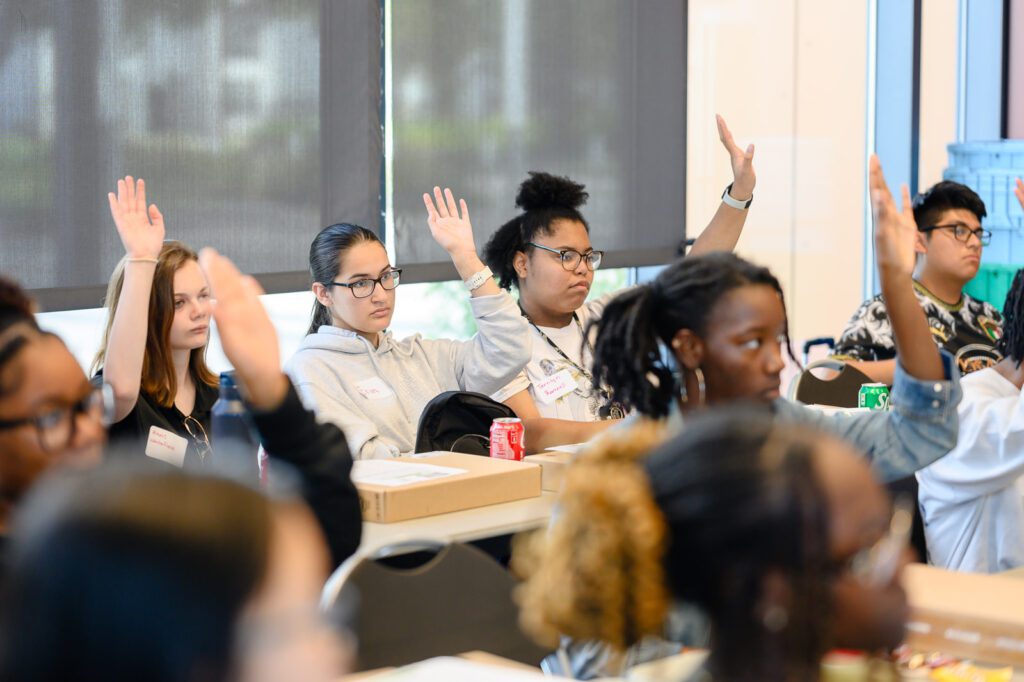 Students raise their hands with questions during the learning session.