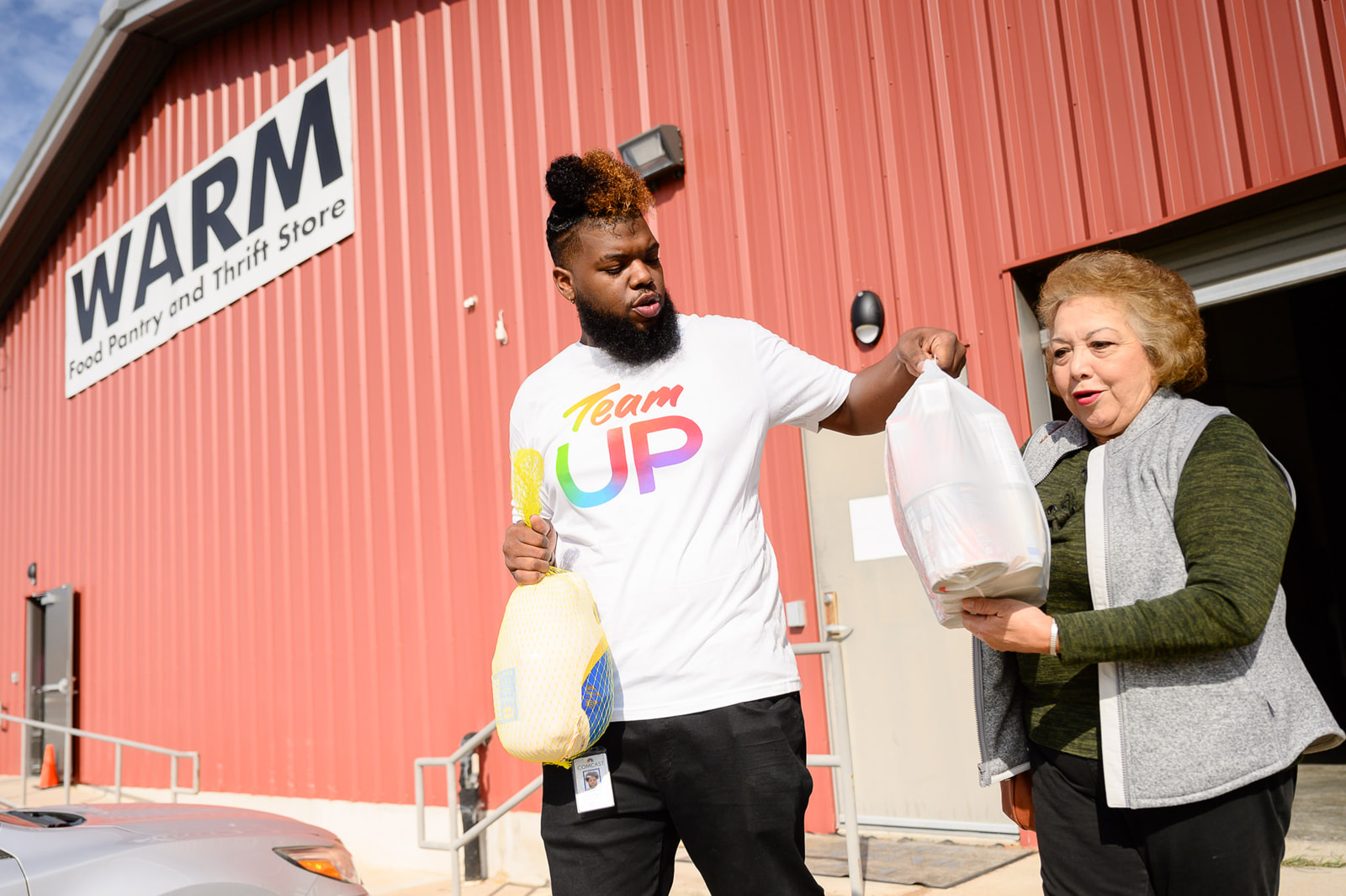 A Team UP volunteer helps carry a turkey and bag for a woman.